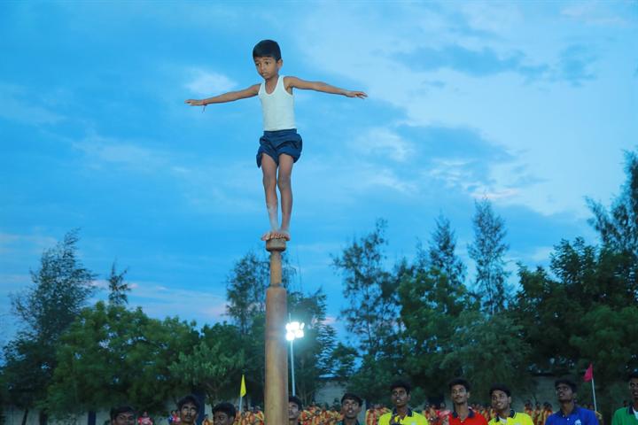 A student balancing on top of a mallakhamb pole