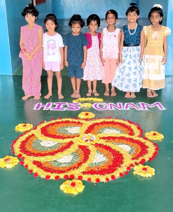 Kindergarten children beside an Onam pookalam